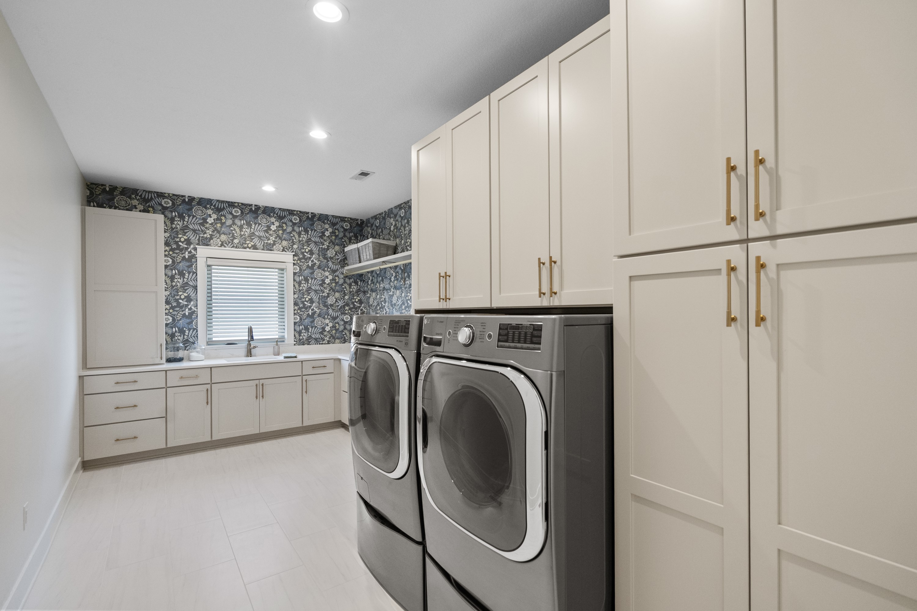Custom laundry room with white cabinetry, floral wallpaper accent, and premium appliances